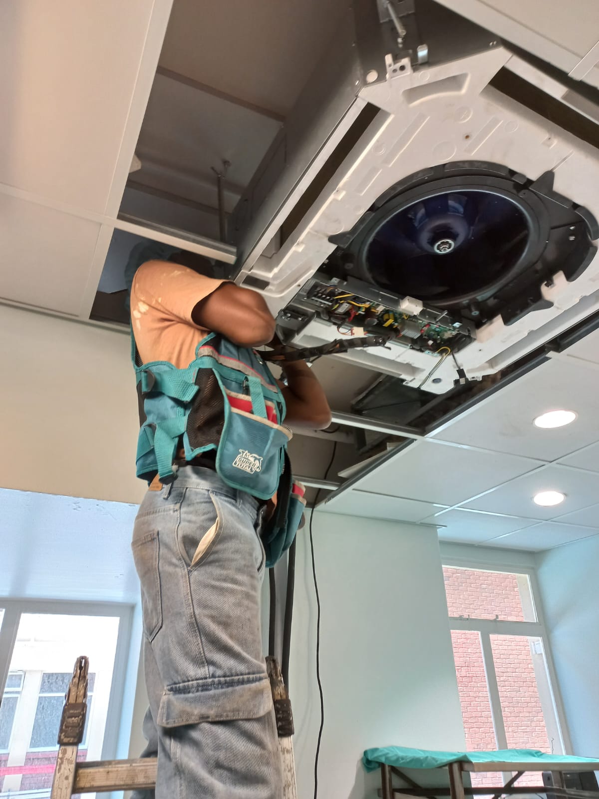 Technician servicing a ceiling cassette air conditioning unit in a hospital sterile department