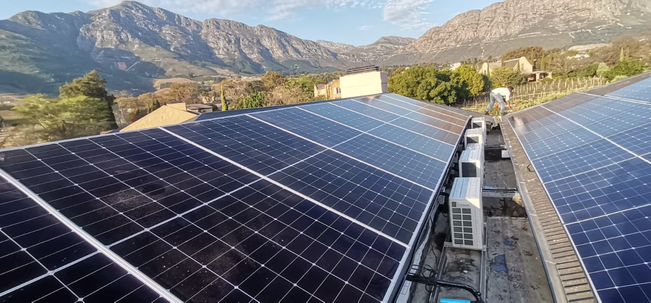 Large solar panel installation on a rooftop with a mountain backdrop, completed by AirTech Solution Systems